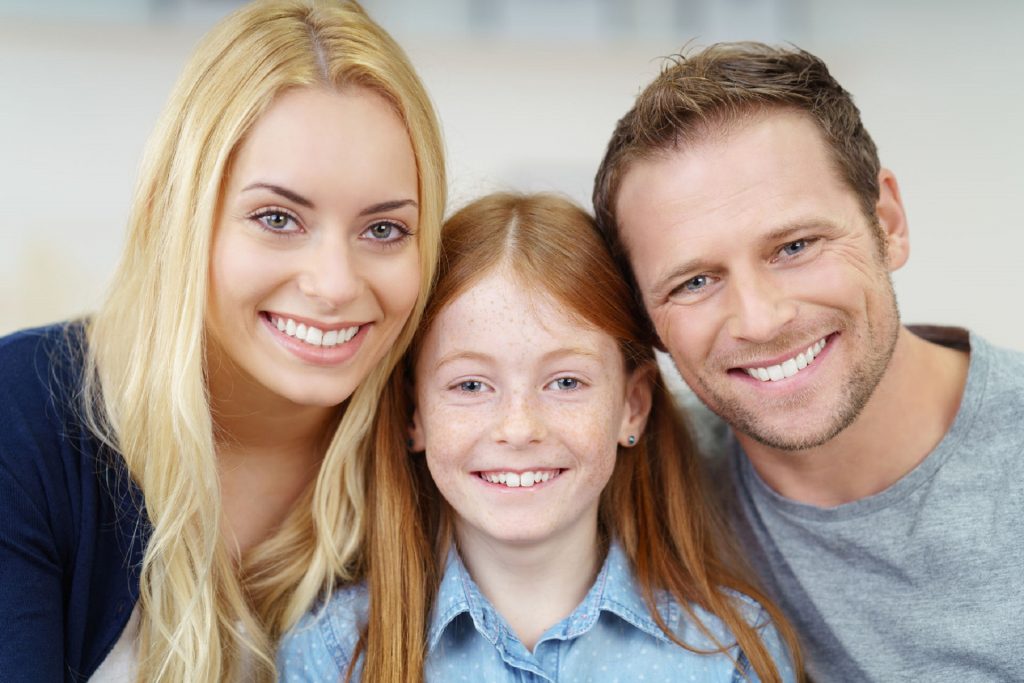 52361627 - smiling portrait of a happy young family with a pretty small redhead girl flanked by her parents posing close together for the camera